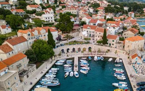 Aerial view of a coastal Mediterranean town with stone houses, quay and small boats in turquoise water