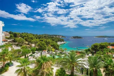Palm trees, green forest and turquoise sea with a beach, pier and boats along the coast