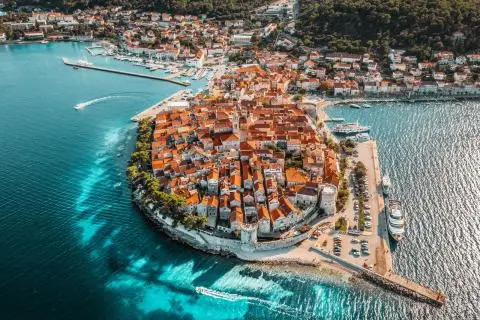 Small fortified peninsula with orange-tiled roofs, marina and yachts along turquoise sea