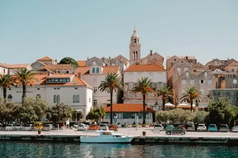 Stone waterfront buildings with palm trees and a white motorboat moored at the quay