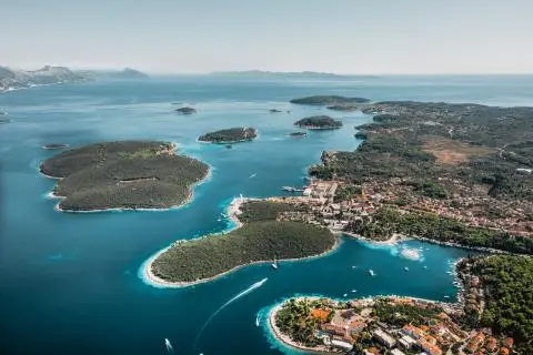 Aerial view of a coastal town with forested islets, turquoise bays and several motorboats