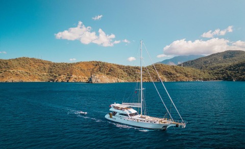 Belgin Sultan sailing yacht anchored near rocky coastline with clear blue water