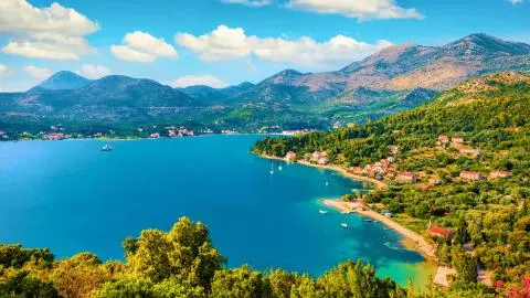 Turquoise bay with small boats, coastal village and green hills under blue sky
