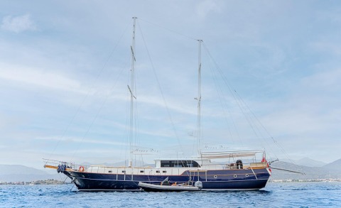 Blue hull gulet yacht anchored in calm sea with a small inflatable boat nearby