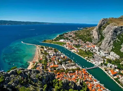 Aerial view of a coastal town with a turquoise bay, canal marina and orange-tiled rooftops