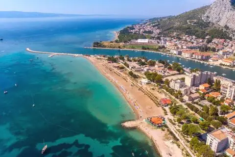 Aerial view of sandy beach extending into turquoise sea with coastal town nearby