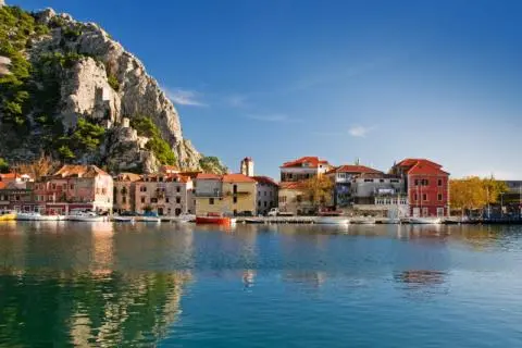Colorful stone waterfront houses, small boats moored in the harbor and a rocky green hill
