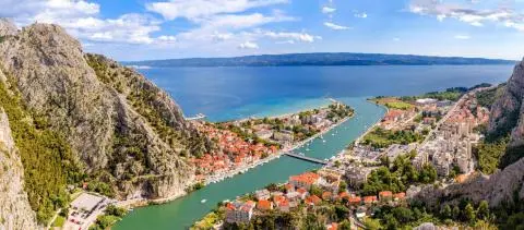 River opening to the sea between rocky mountains, red-roofed town and moored boats