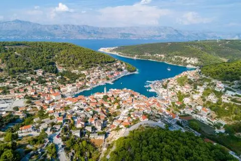 Harbor town with red-roofed houses, green hills and a narrow blue inlet seen from above