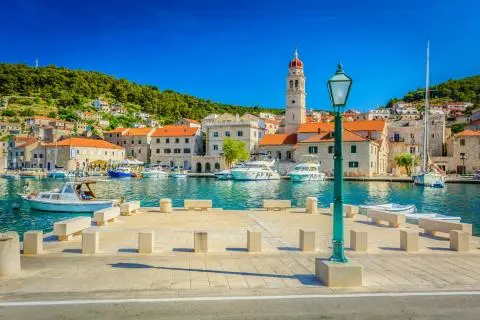 Harbor promenade with a green streetlamp, moored yachts and stone houses with red roofs