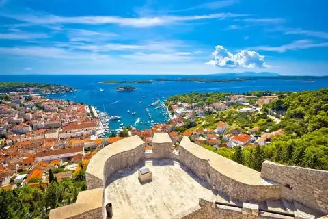 View from stone terrace over an Adriatic harbor with boats, islands and red-tiled town