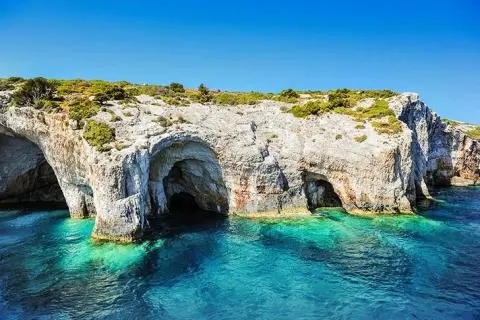 White rocky coastline with sea caves and turquoise clear water under blue sky