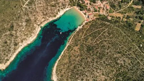 Aerial bay view with turquoise shallow water, a small boat in the cove and buildings on shore