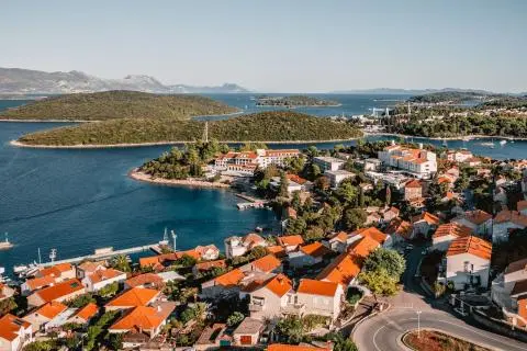 Panoramic view of red-tiled roofs, coastal town and green islets in deep blue sea