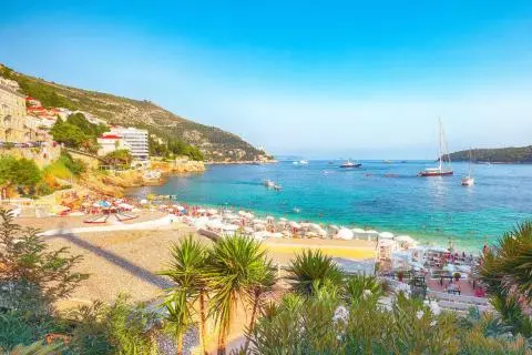 Coastal beach with umbrellas and sunbeds, several anchored sailboats and motorboats