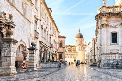 Stone-paved square with historic stone buildings, a domed church and a few pedestrians
