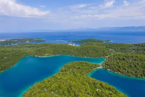 Forest-covered coves and small islands with deep blue sea under a partly cloudy sky