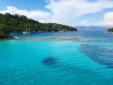 Turquoise sea with a two-masted sailing gulet near a pine‑covered island under a blue sky