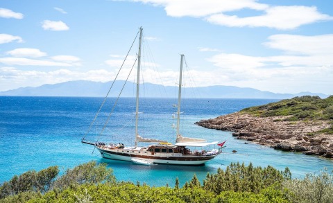 Two-masted sailing yacht anchored in turquoise sea near rocky coast