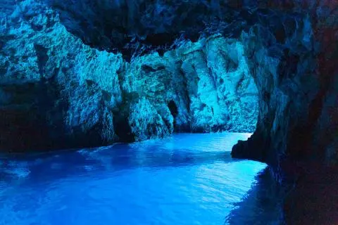 Sea water glowing electric blue inside a rocky sea cave illuminated by blue light