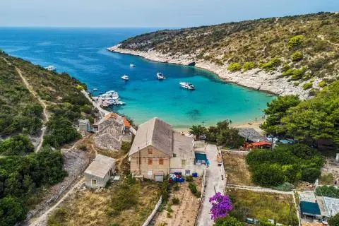 Turquoise bay with several small yachts at anchor, stone houses on shore and pine-covered hills