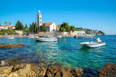 Coastal church bell tower with small boats moored in clear turquoise water