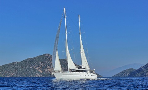 Angelo II sailing yacht with white hull and twin masts on calm blue sea near rocky islands