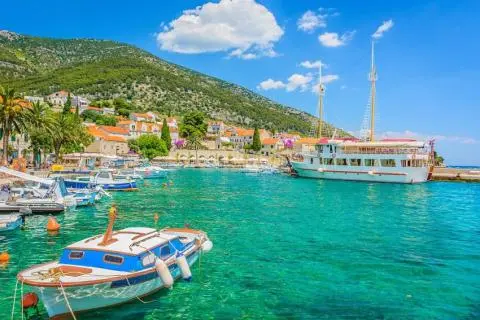 Small and large boats moored in turquoise harbor with coastal village houses and green hillside