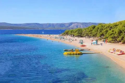 Pebble spit beach with sunbathers, a yellow watercraft moored and turquoise sea view