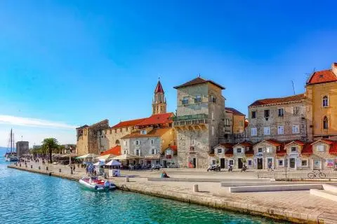 Marina with stone buildings and red-roofed tower, people on the promenade and a small boat moored
