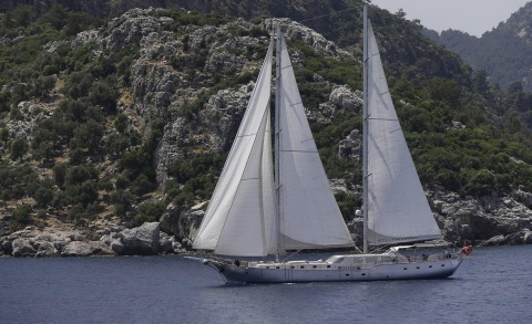 Silver Moon sailing near rocky coastline with white sails unfurled