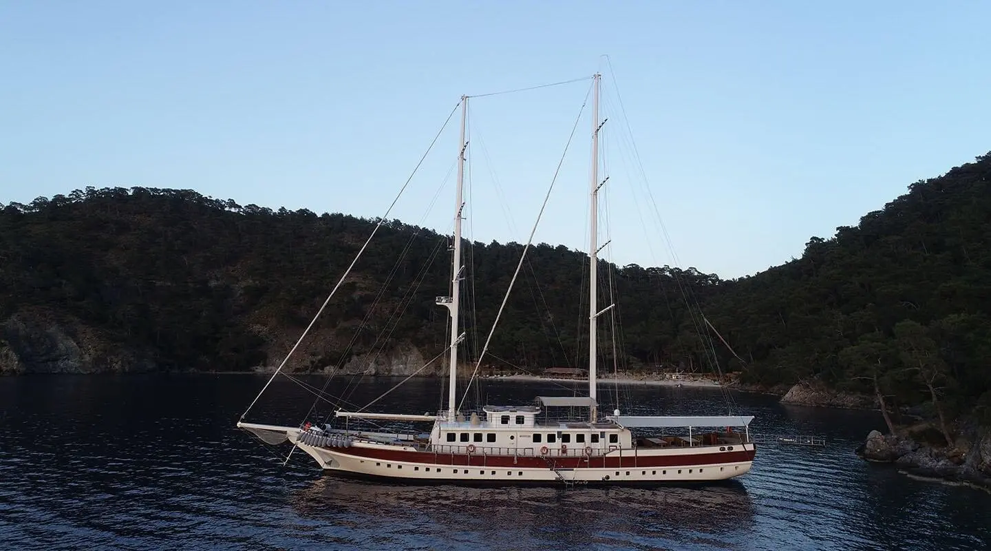 Gulet Tersane 8 anchored near hillside, two masts, dark hull, calm sea