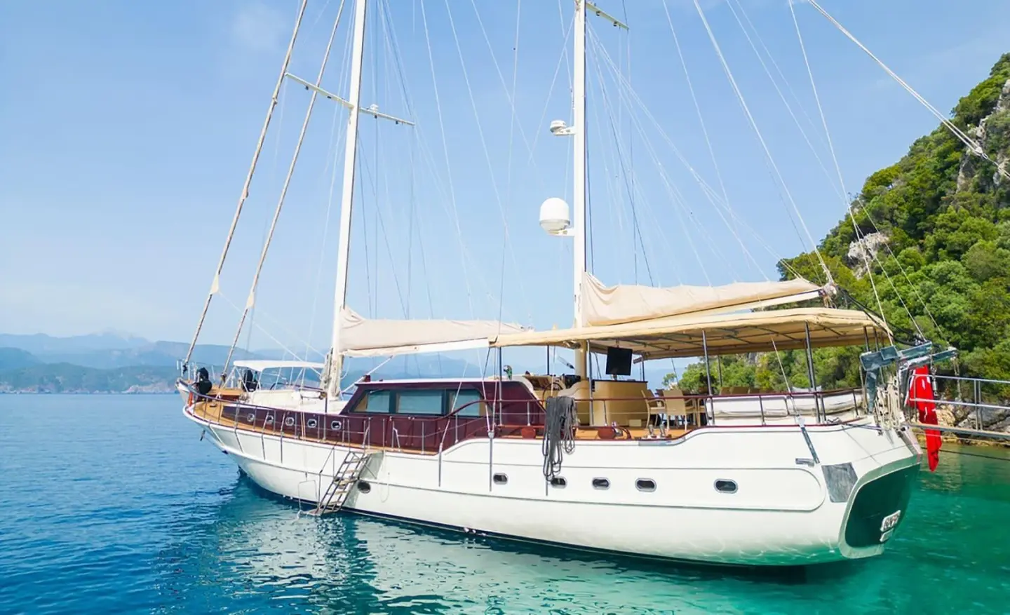 Yacht Mein Schatz anchored near a beach with sunlit deck and sails