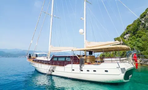 Yacht Mein Schatz anchored near a beach with sunlit deck and sails