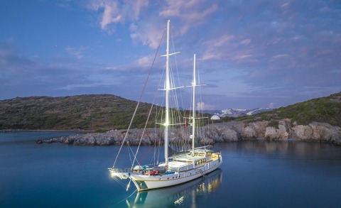 Sailing yacht Lucky You with tall masts docked in calm blue water at sunset