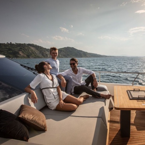 Man in sunglasses, woman and boy relaxing on yacht deck with sea and coastline