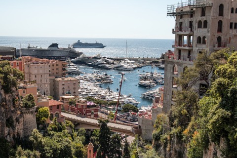 Harbor crowded with yachts, coastal buildings and a cruise ship visible on the open sea