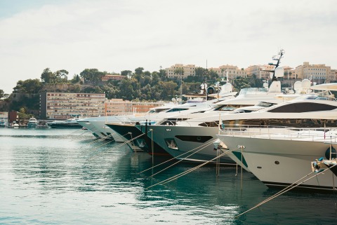 Row of luxury motor yachts moored bow-first at a marina with waterfront buildings