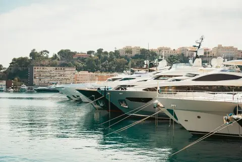 Row of luxury motor yachts moored bow-first at a marina with waterfront buildings