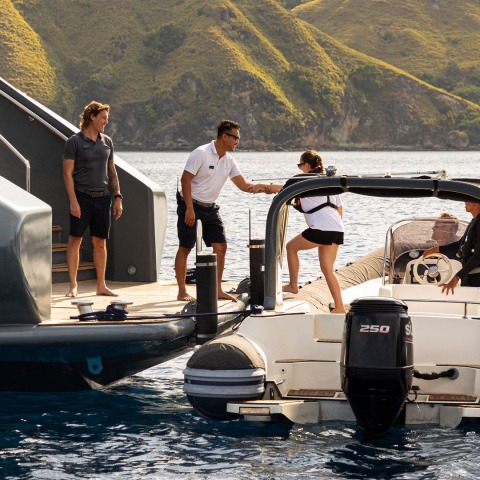 Crew member reaching from a small RIB to help a passenger onto a luxury yacht platform
