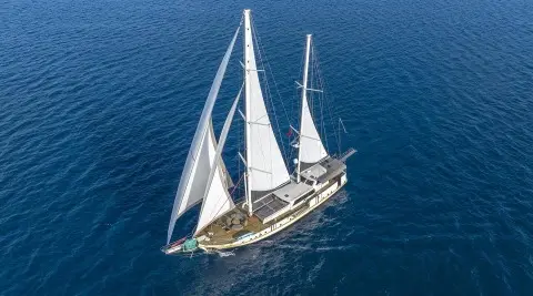 A gulet sailing with three masts on blue sea, viewed from above