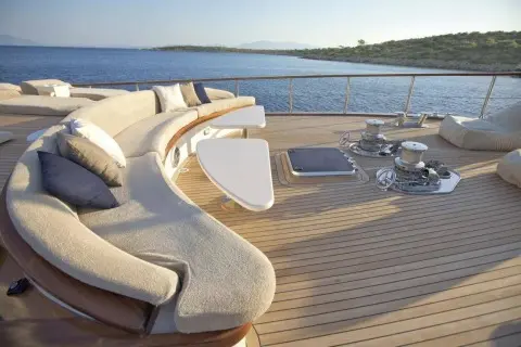 Curved beige sofa with cushions on teak deck overlooking calm sea and distant shore