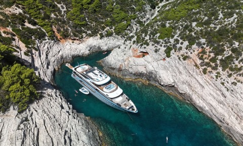 Luxury motor yacht anchored in a rocky cove with inflatable tenders and turquoise water