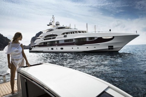 A white luxury yacht anchored at sea with a woman in white standing on a nearby boat