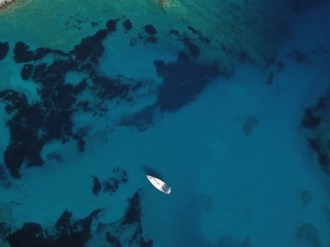 Aerial view of a single white yacht anchored in deep blue water with dark seafloor patches