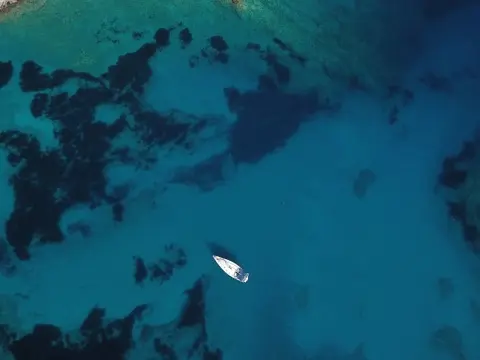 Aerial view of a single white yacht anchored in deep blue water with dark seafloor patches