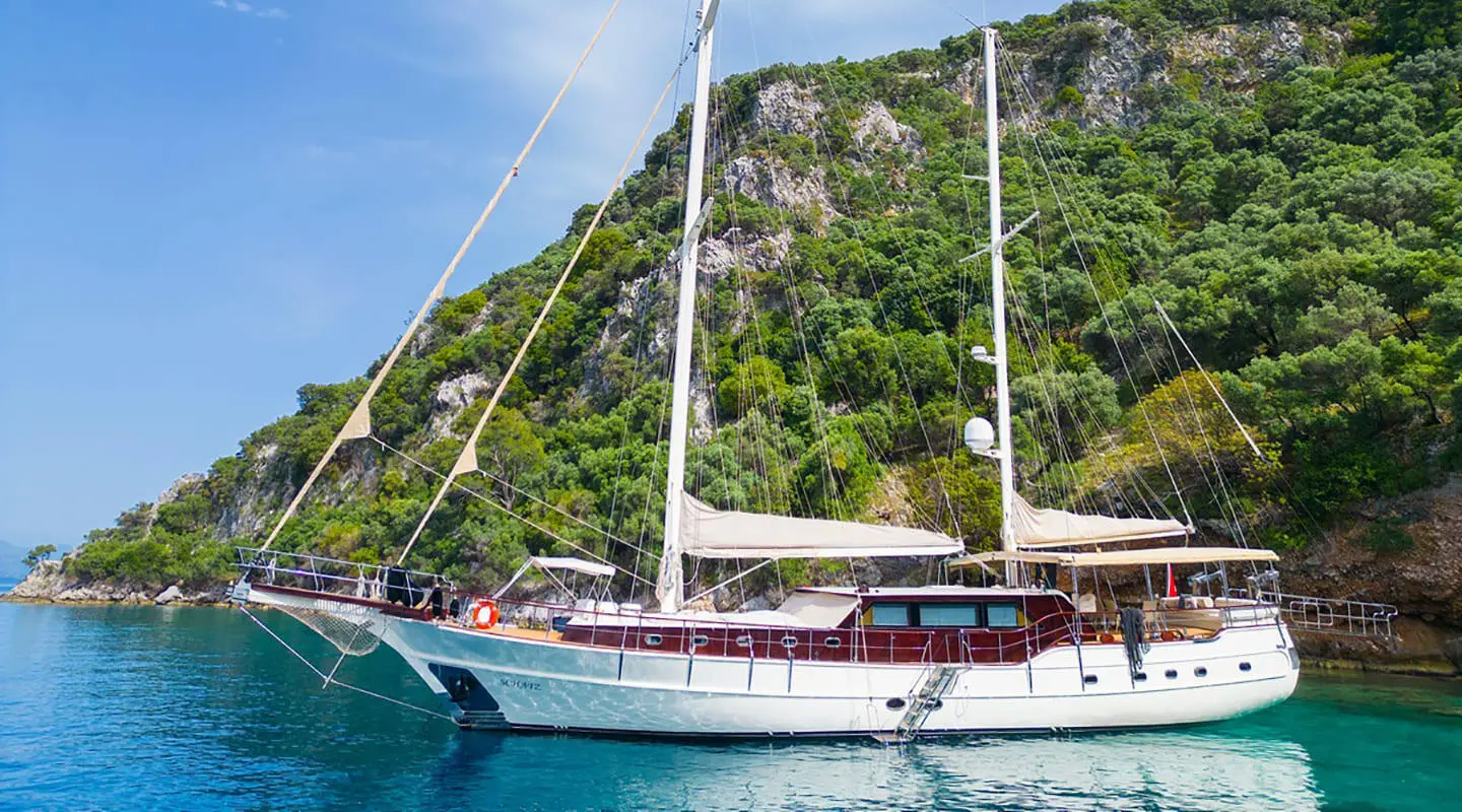 Two-masted luxury gulet yacht anchored in turquoise sea near rocky shoreline