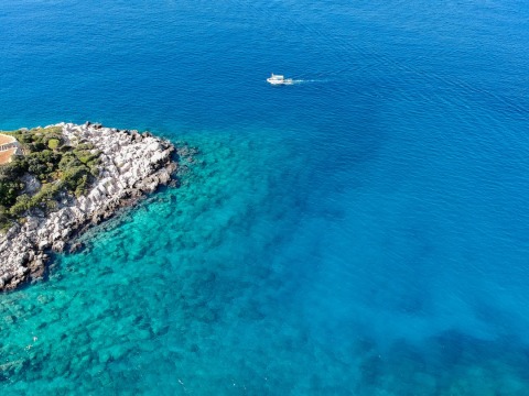Rocky shoreline with pine trees and a small boat on vivid turquoise-blue sea