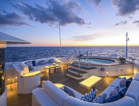 Luxury yacht deck at sunset with a circular jacuzzi, seating areas and ambient lighting