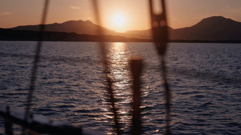 Sunset seen from a sailboat, sun reflecting on rippled sea with silhouetted mountains